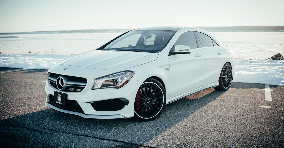 Sleek white Mercedes Benz sedan parked on a snowy road with a tranquil background.