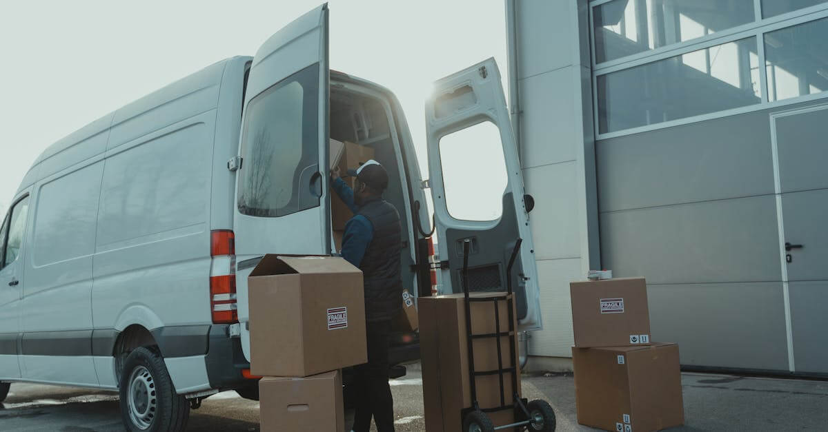 Courier loading cardboard boxes into a delivery van outside a warehouse.