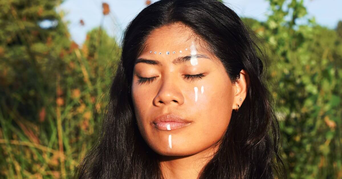 Calm young woman with tribal face paint enjoying sunlight in serene outdoor environment.