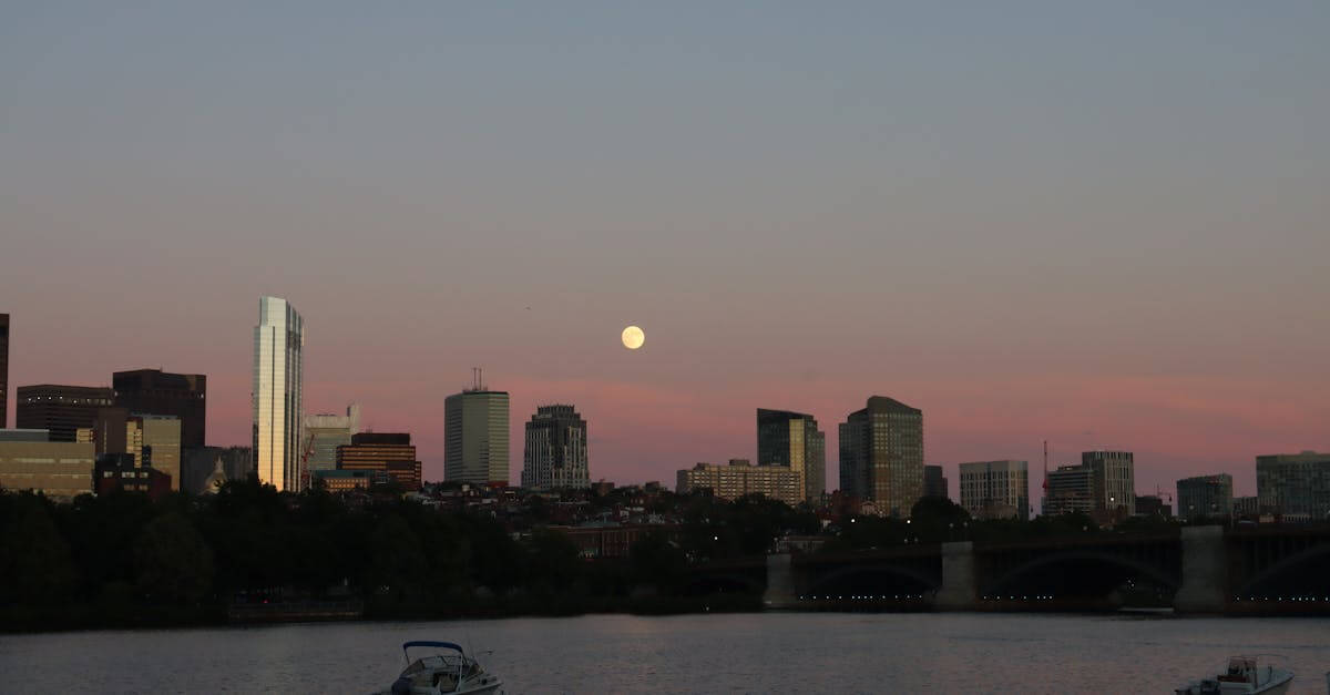 Scenic view of Boston skyline and Charles River at dusk with a full moon backdrop.