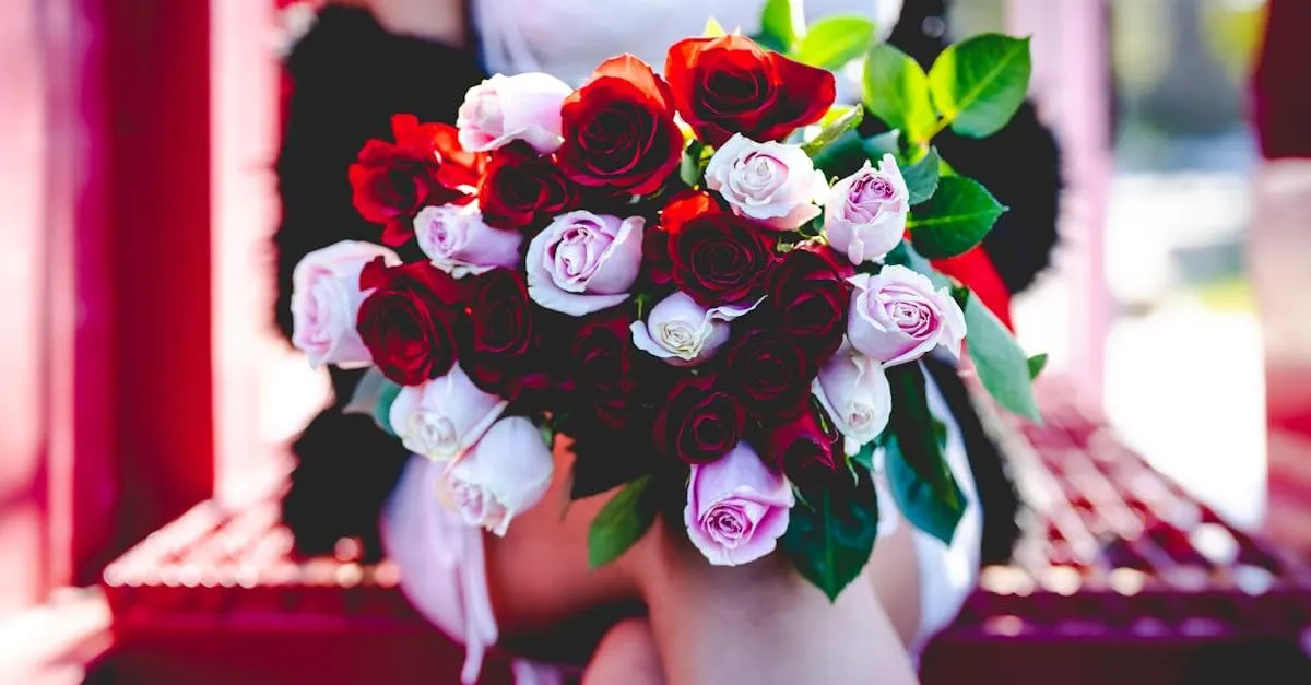 Beautiful bride holding a bouquet of red and pink roses with lush greenery outdoors.