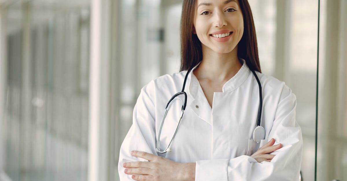 Portrait of a smiling female doctor with arms crossed and stethoscope in a hospital corridor.