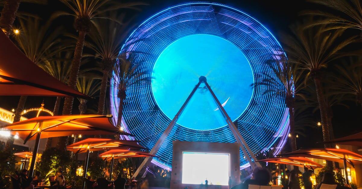 Night view of a brightly lit Ferris wheel surrounded by tropical trees at Irvine Spectrum Center.