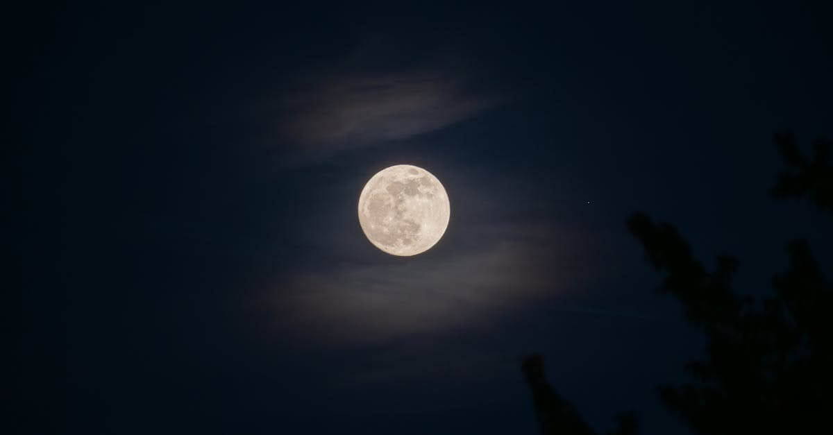 A serene full moon glowing amidst subtle clouds in a night sky.