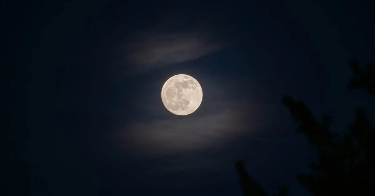 A serene full moon glowing amidst subtle clouds in a night sky.