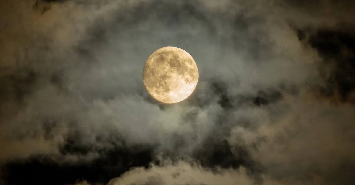 A mesmerizing full moon shining through a cloudscape in a dark, captivating night sky.