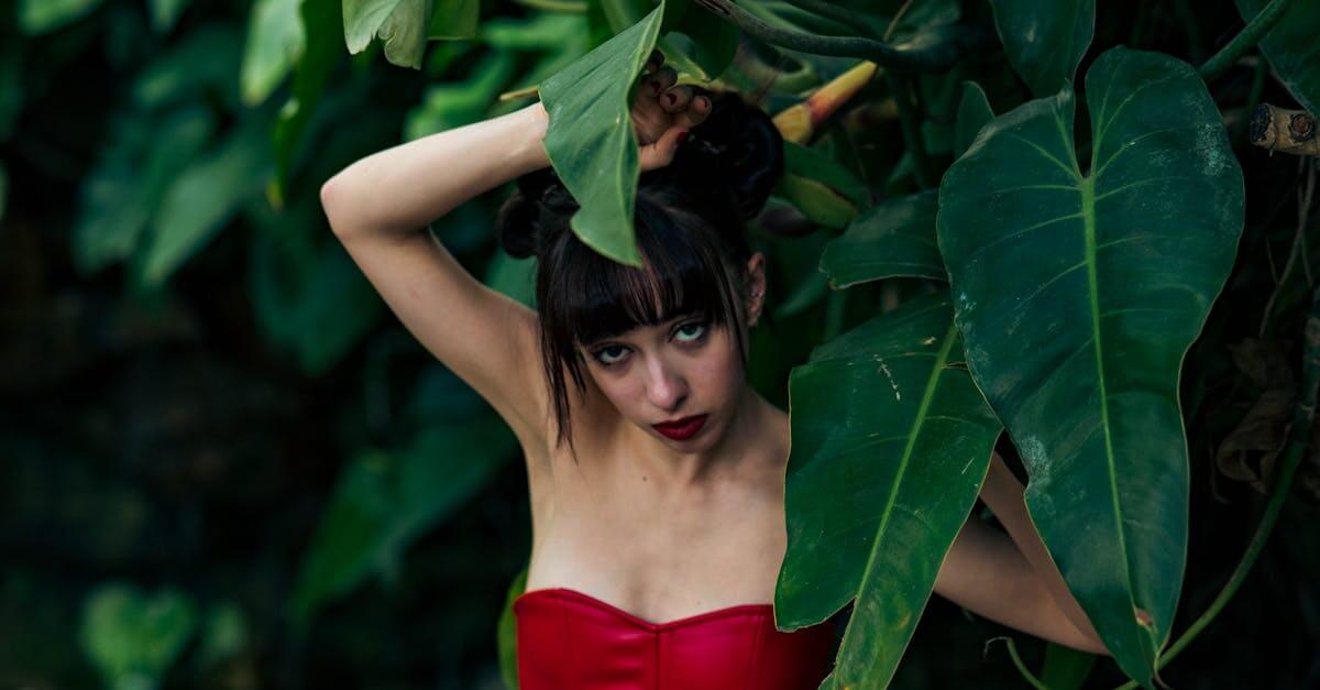 Striking fashion portrait in nature with vibrant red dress and lush green background.