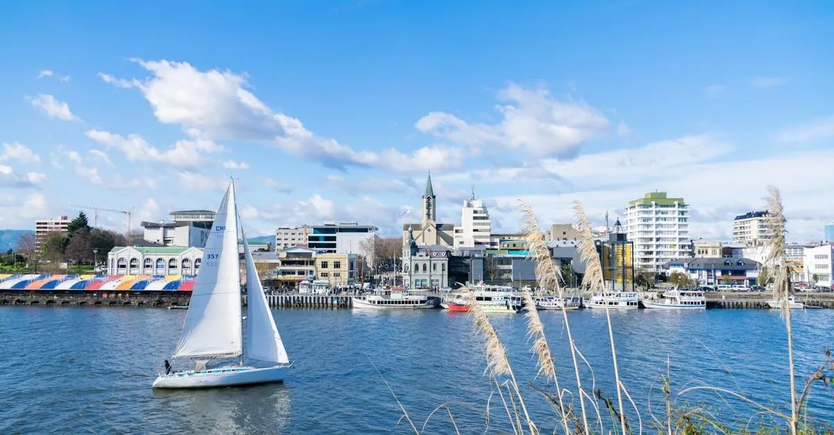 Beautiful day at the Valdivia waterfront in Chile, featuring a sailboat and urban skyline.