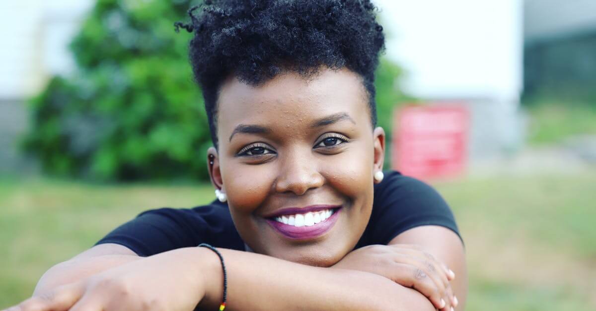 Cheerful young woman with curly black hair smiling outdoors in Lewiston, Maine.