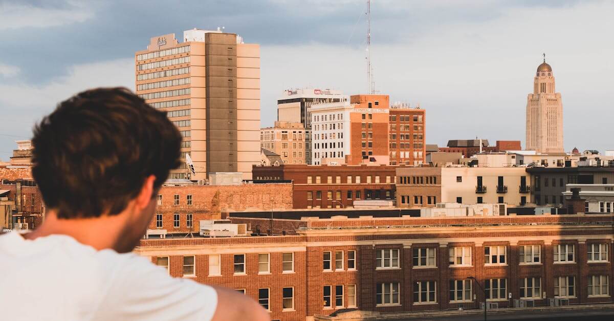 Skyline of Lincoln, NE with a man observing at sunset, featuring the State Capitol.