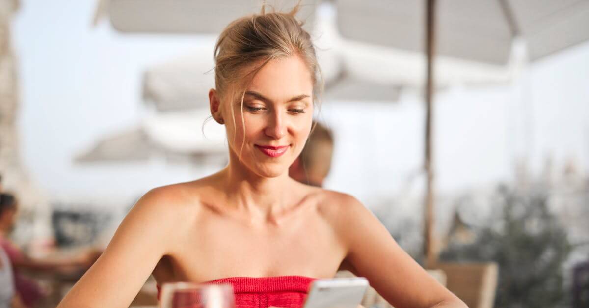Smiling woman enjoying leisure time with smartphone at an outdoor cafe.