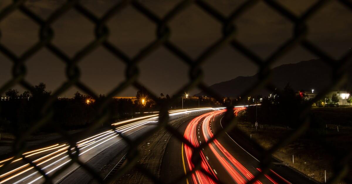 Night long exposure capturing car light trails through a chain link fence in Moreno Valley, CA.