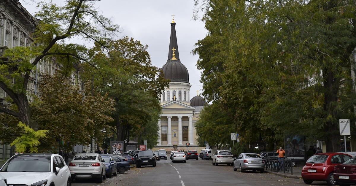 Street view of a cathedral in Odessa, Ukraine with cars parked and trees lining the road.