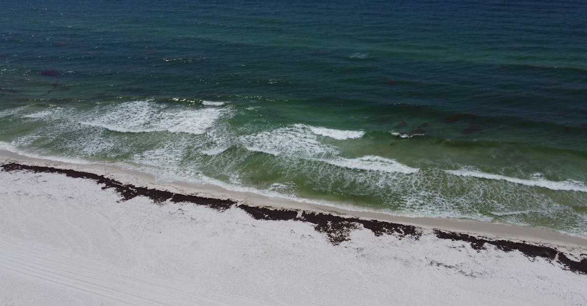 Aerial view of the pristine Pensacola Beach with waves crashing onto the shore under a summer sky.