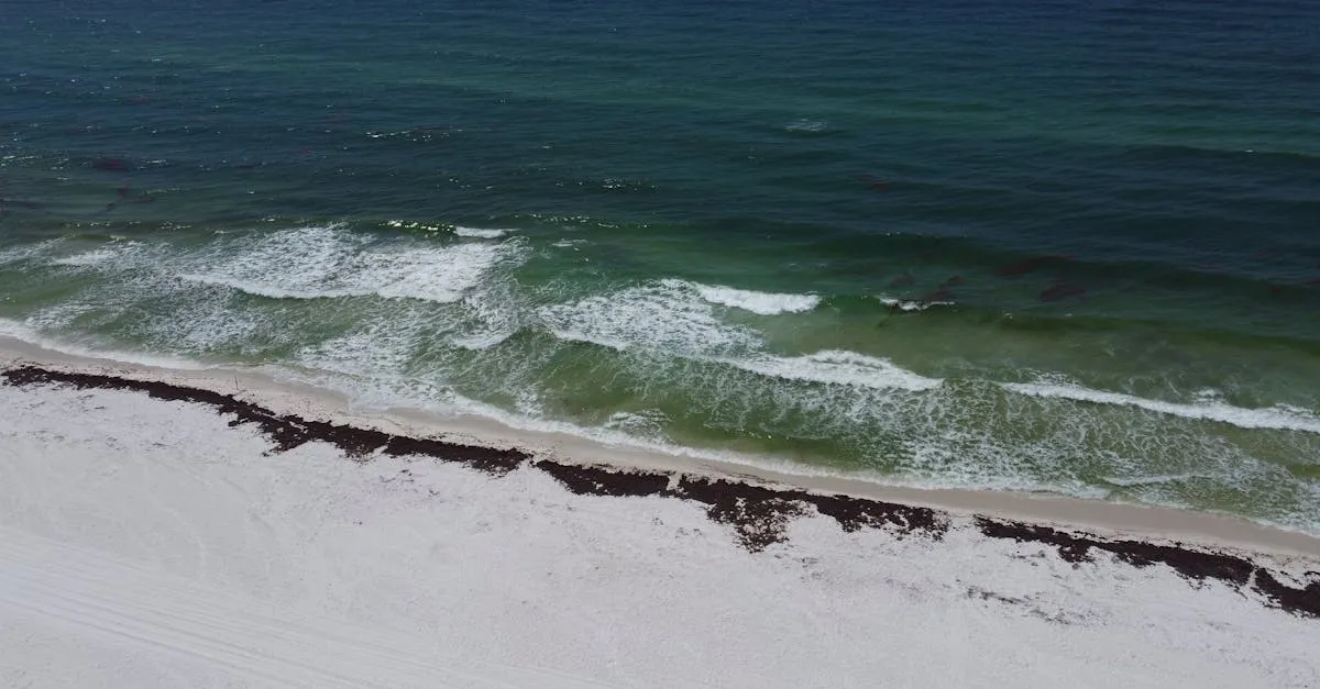 Aerial view of the pristine Pensacola Beach with waves crashing onto the shore under a summer sky.