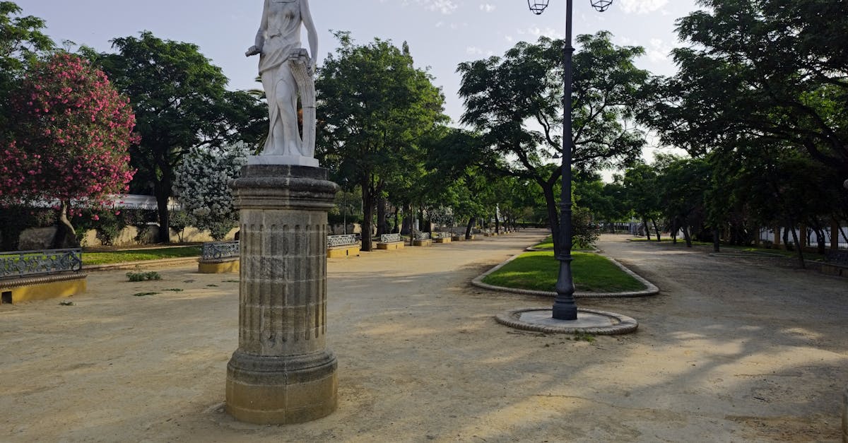 Serene park scene in El Puerto de Santa María featuring a classical statue with trees and lamp posts.