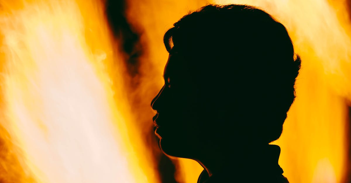 A dramatic silhouette of a person's profile against vivid orange flames.
