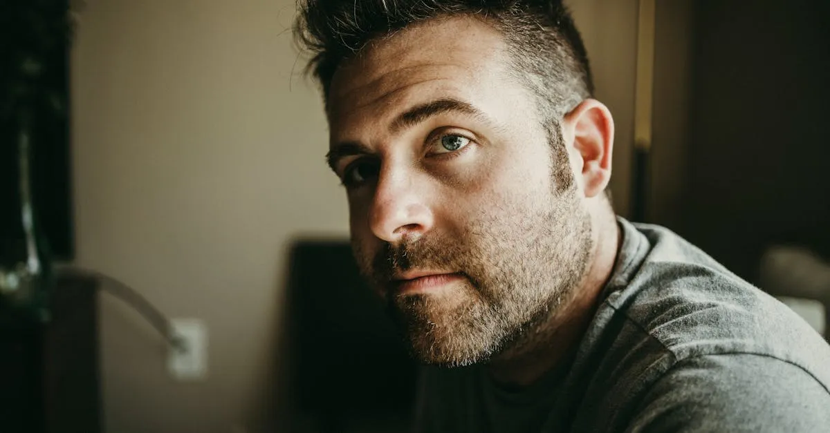 Close-up portrait of a thoughtful bearded man indoors with moody lighting.